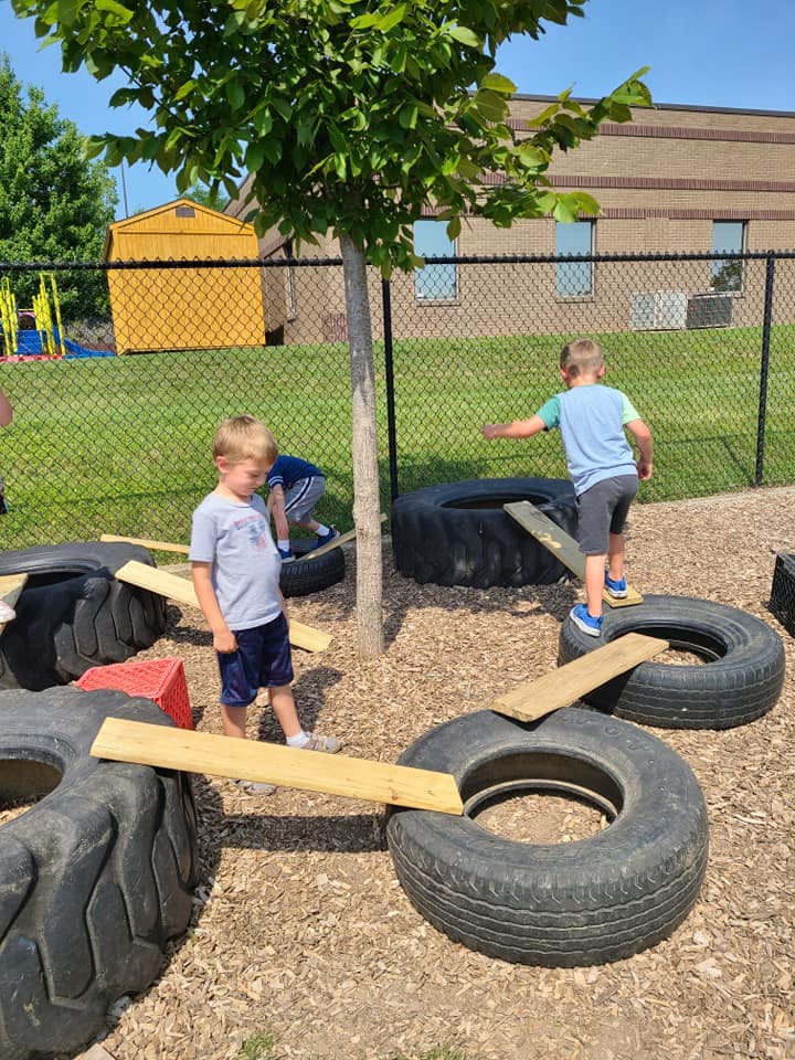 Children playing on tires and wooden planks outdoors