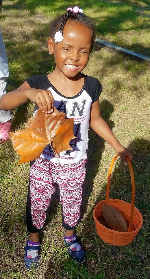 Child holding a large brown leaf and a basket with an object in it
