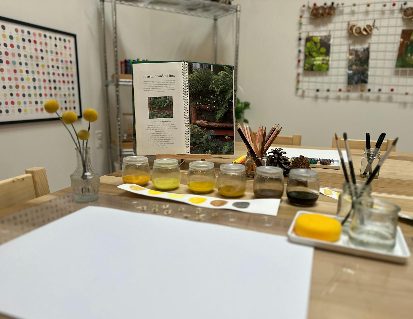 Art supplies on a table, including jars of paint, brushes, and paper