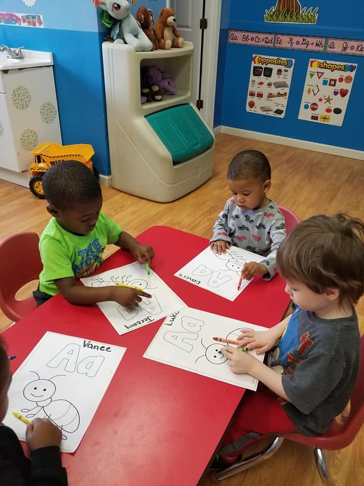 Three children coloring at a red table in a classroom