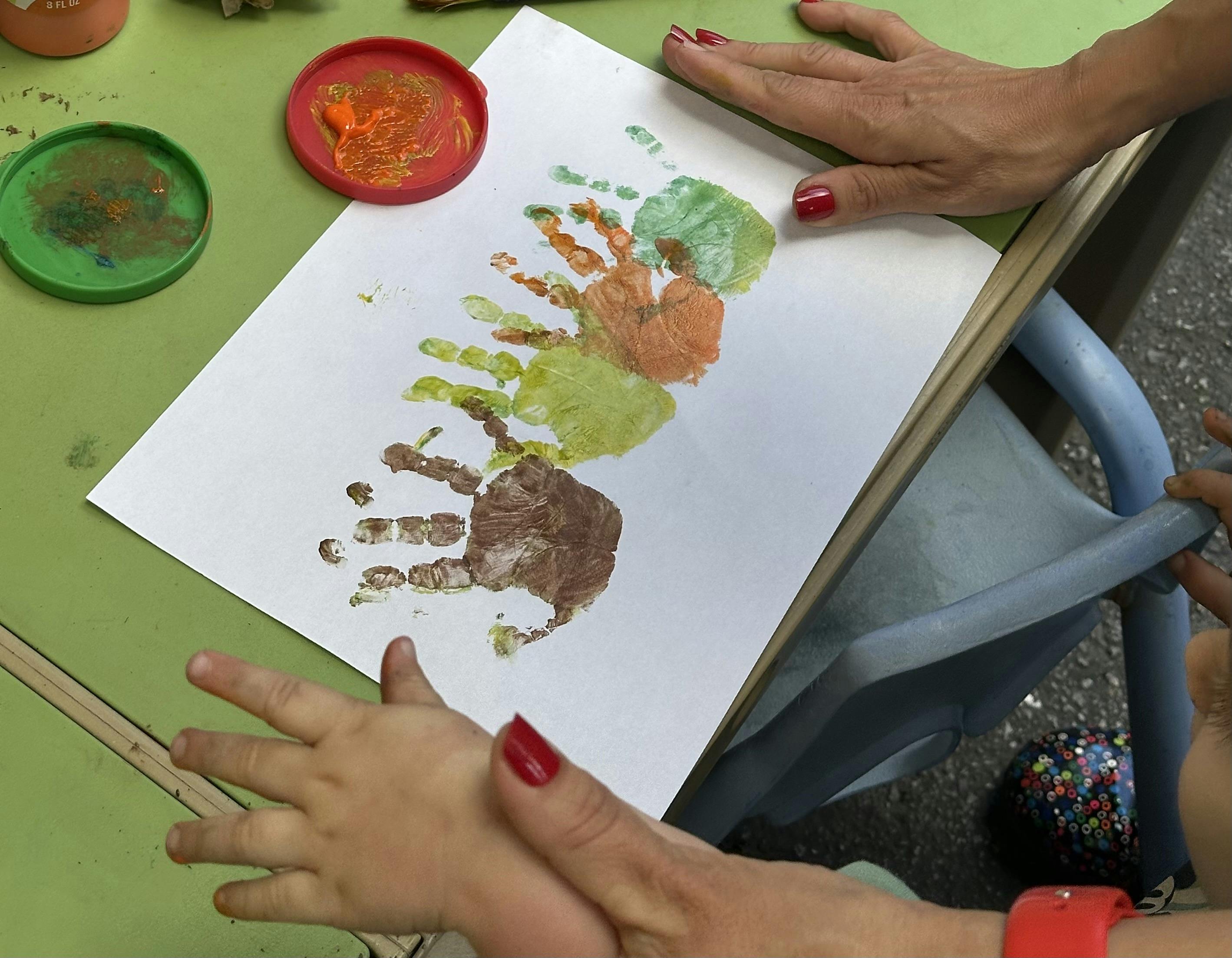 Adult and child hands making colorful handprints on paper