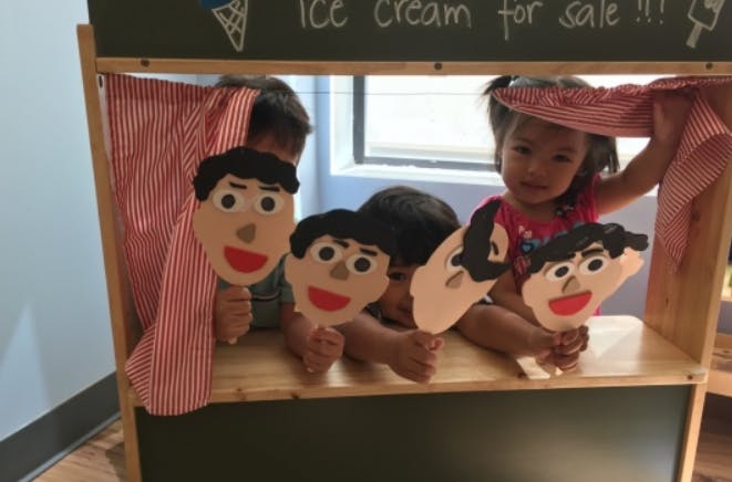 Children playing with puppet faces behind a puppet stand