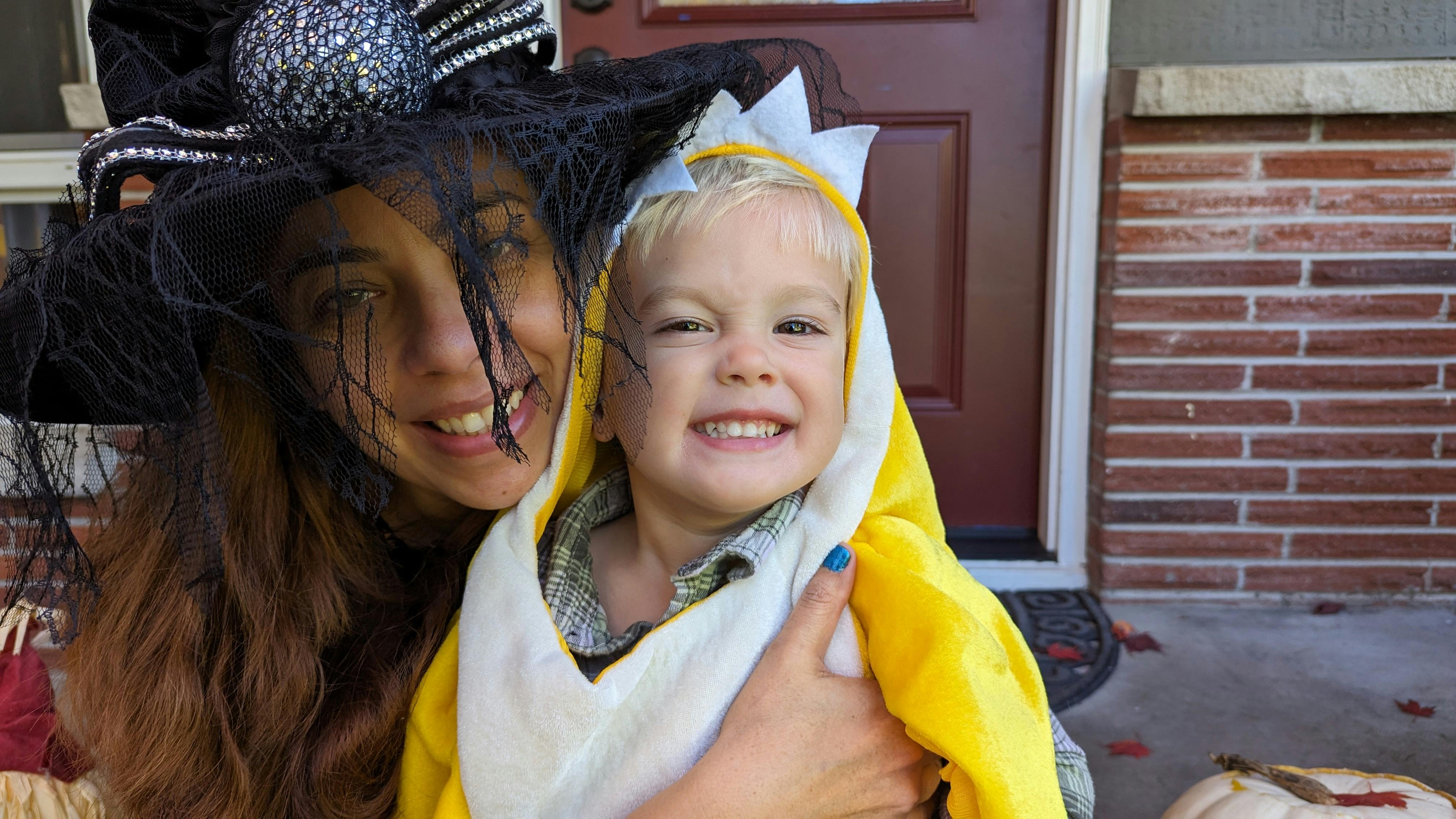 Person in witch hat holding a child in a yellow costume