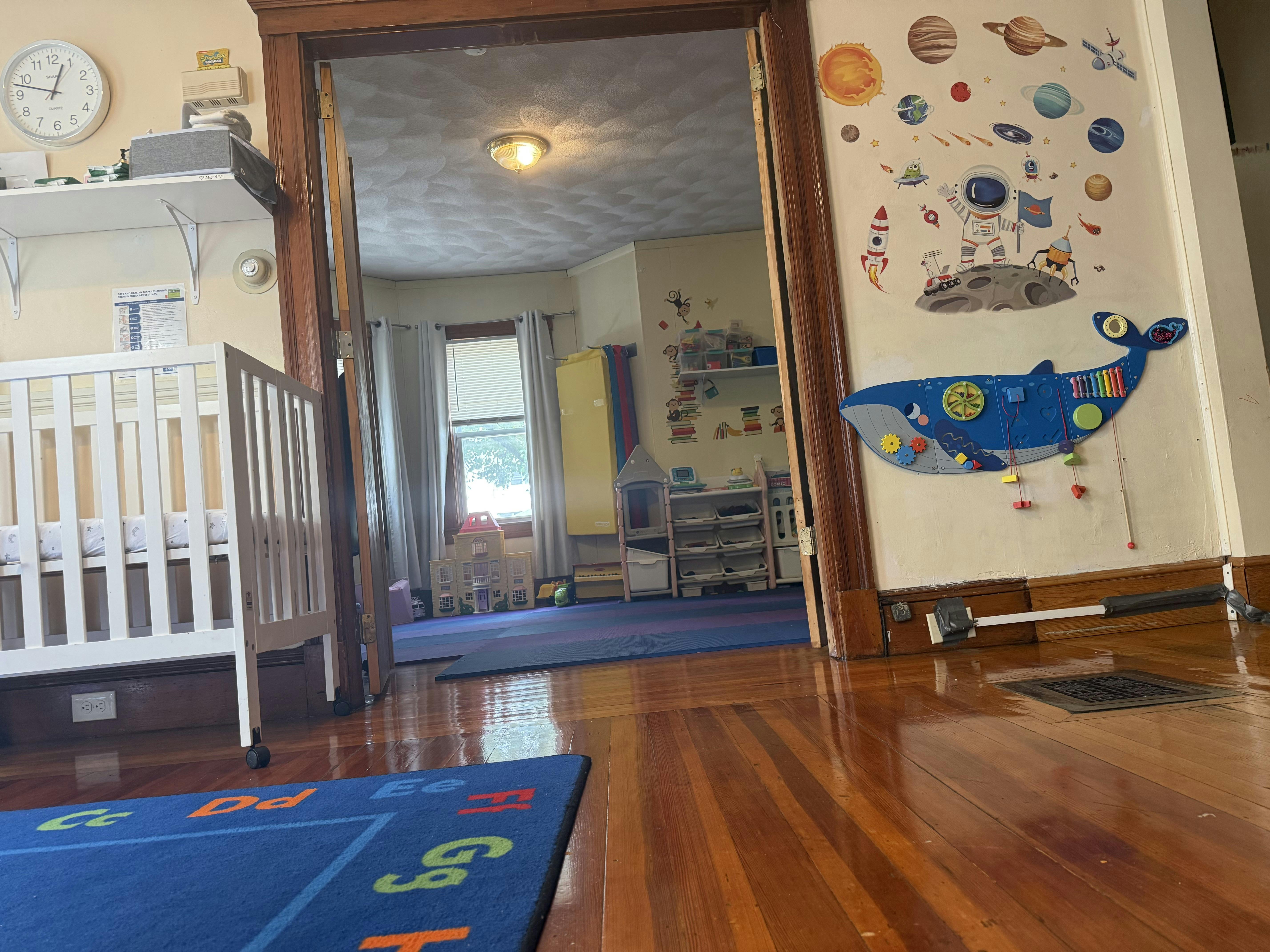 Childcare room with a crib, toys, and space-themed wall decals