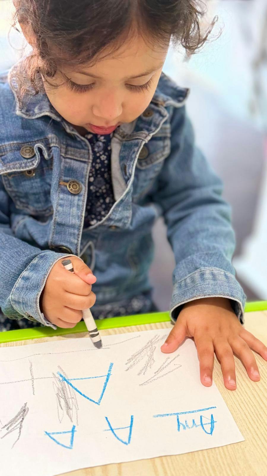 Child drawing letters on a sheet of paper with a crayon