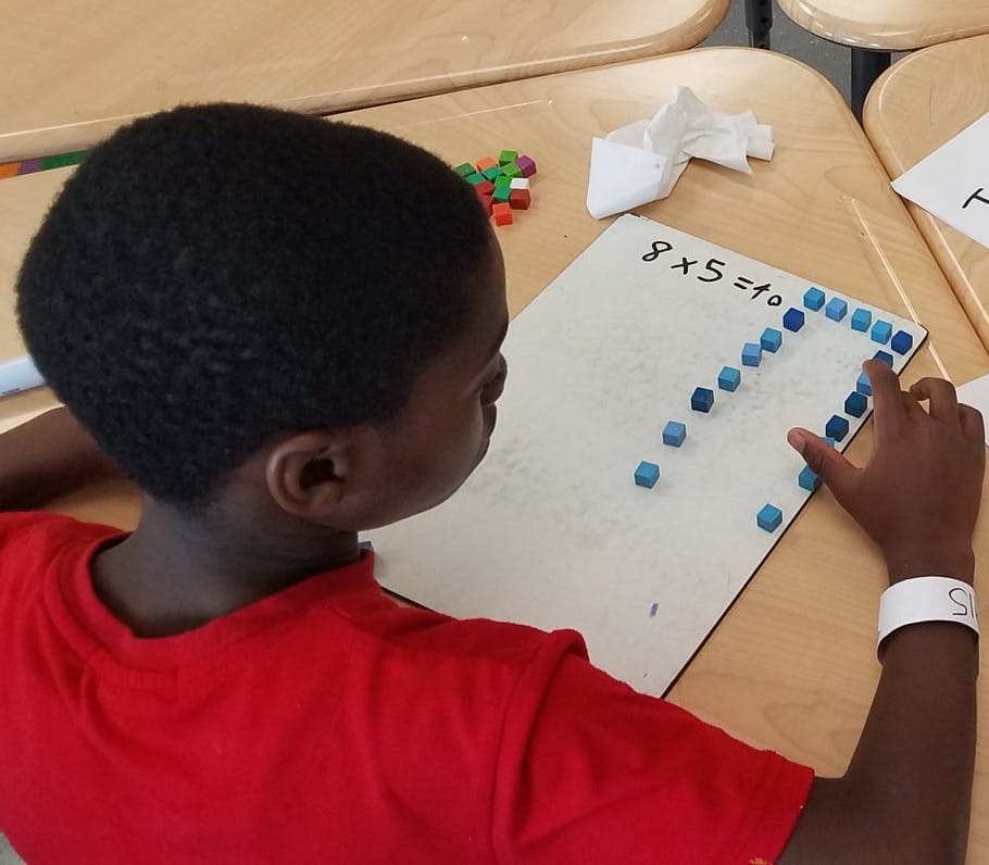 Child working on a math problem with small blue blocks
