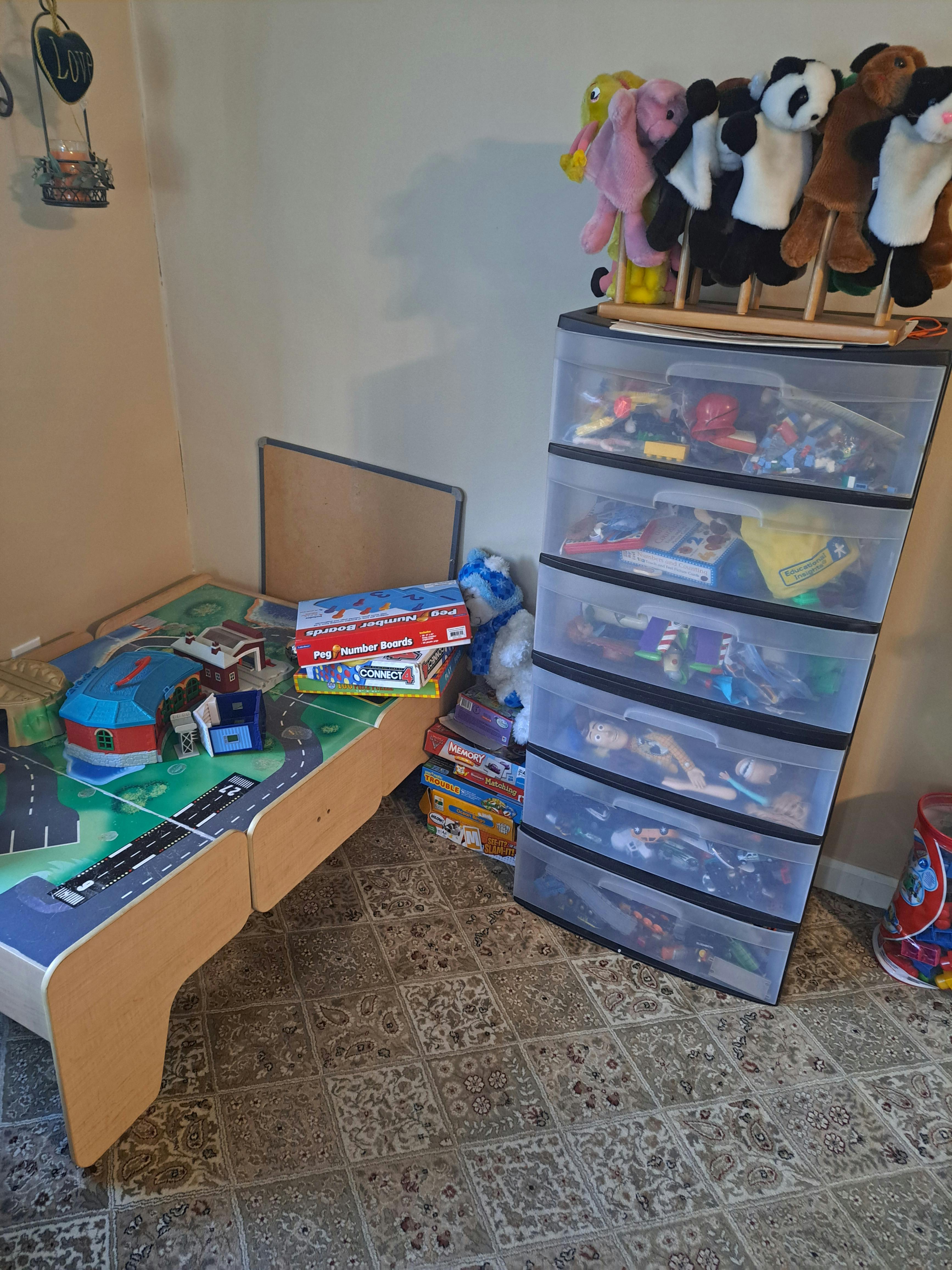 Play table with toy cars and buildings, storage drawers with toys, and puppets