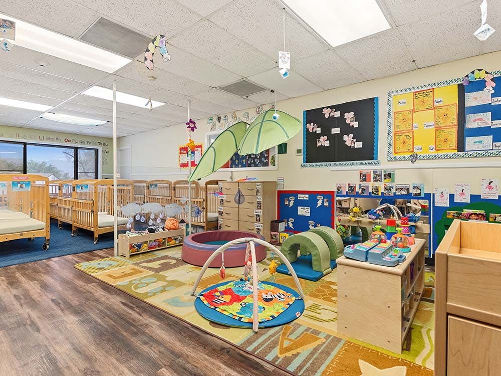 A colorful playroom with cribs, play mats, and learning materials