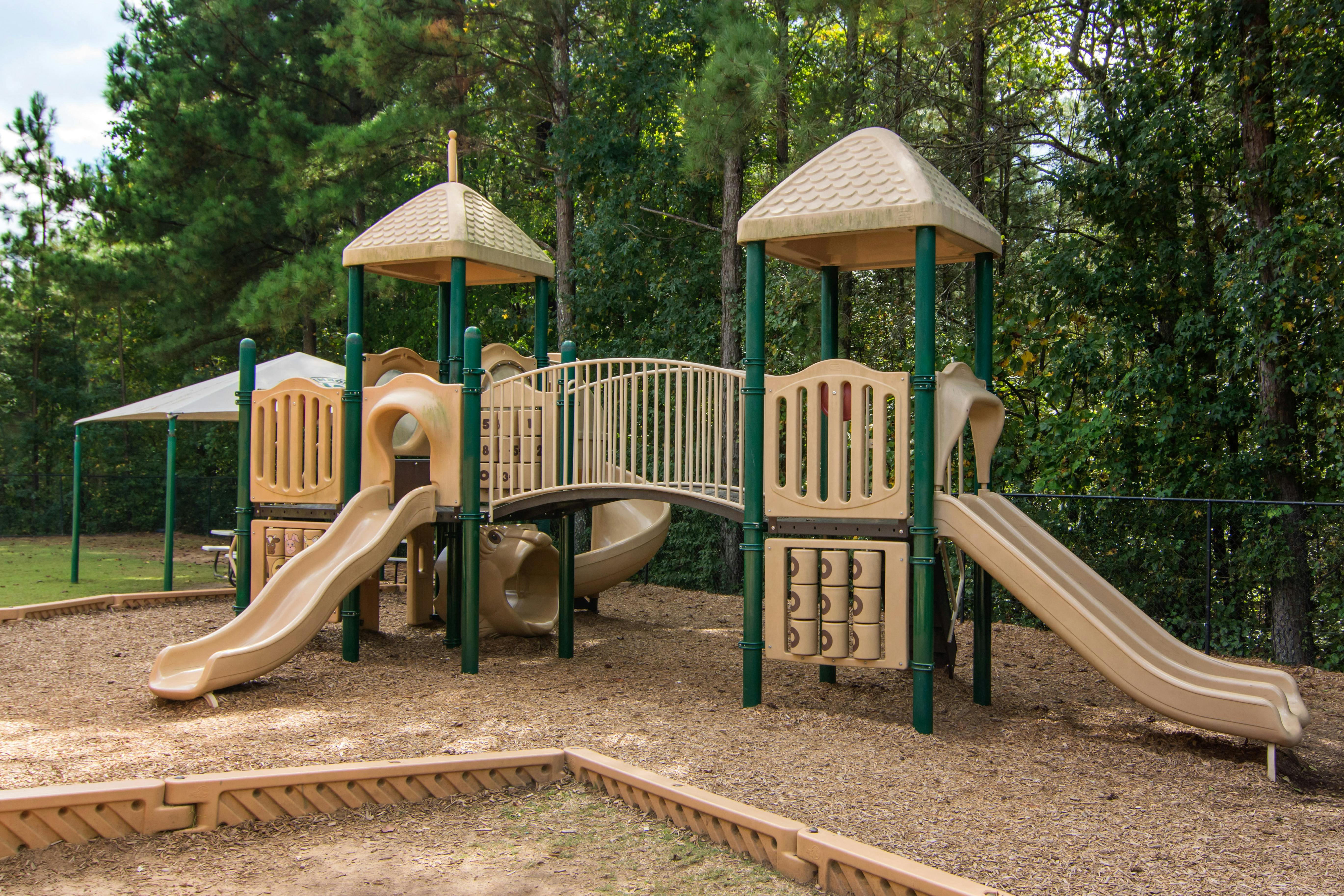 Empty children's playground with multiple slides and a bridge surrounded by trees
