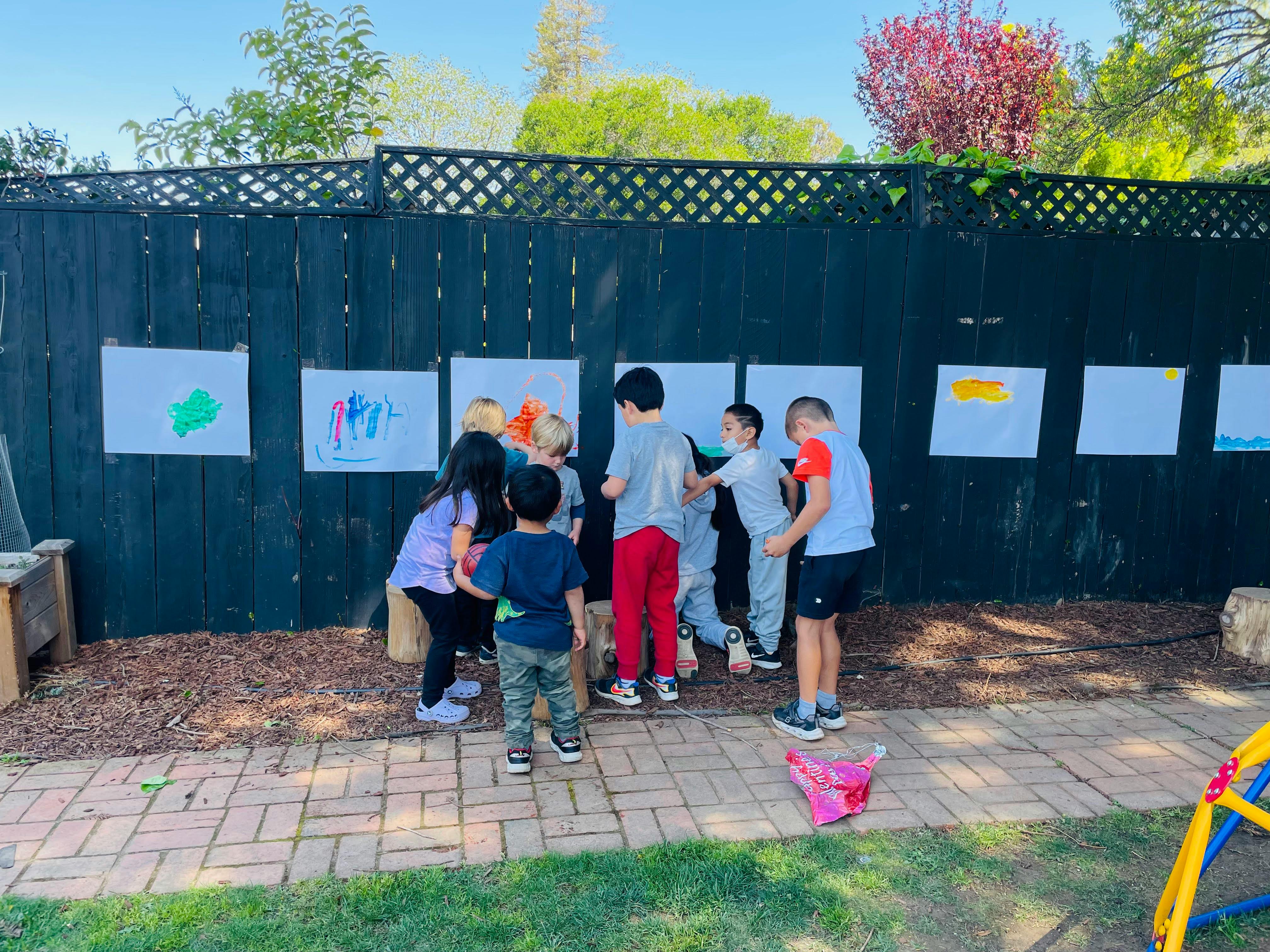 Children gathered around artwork displayed on a fence