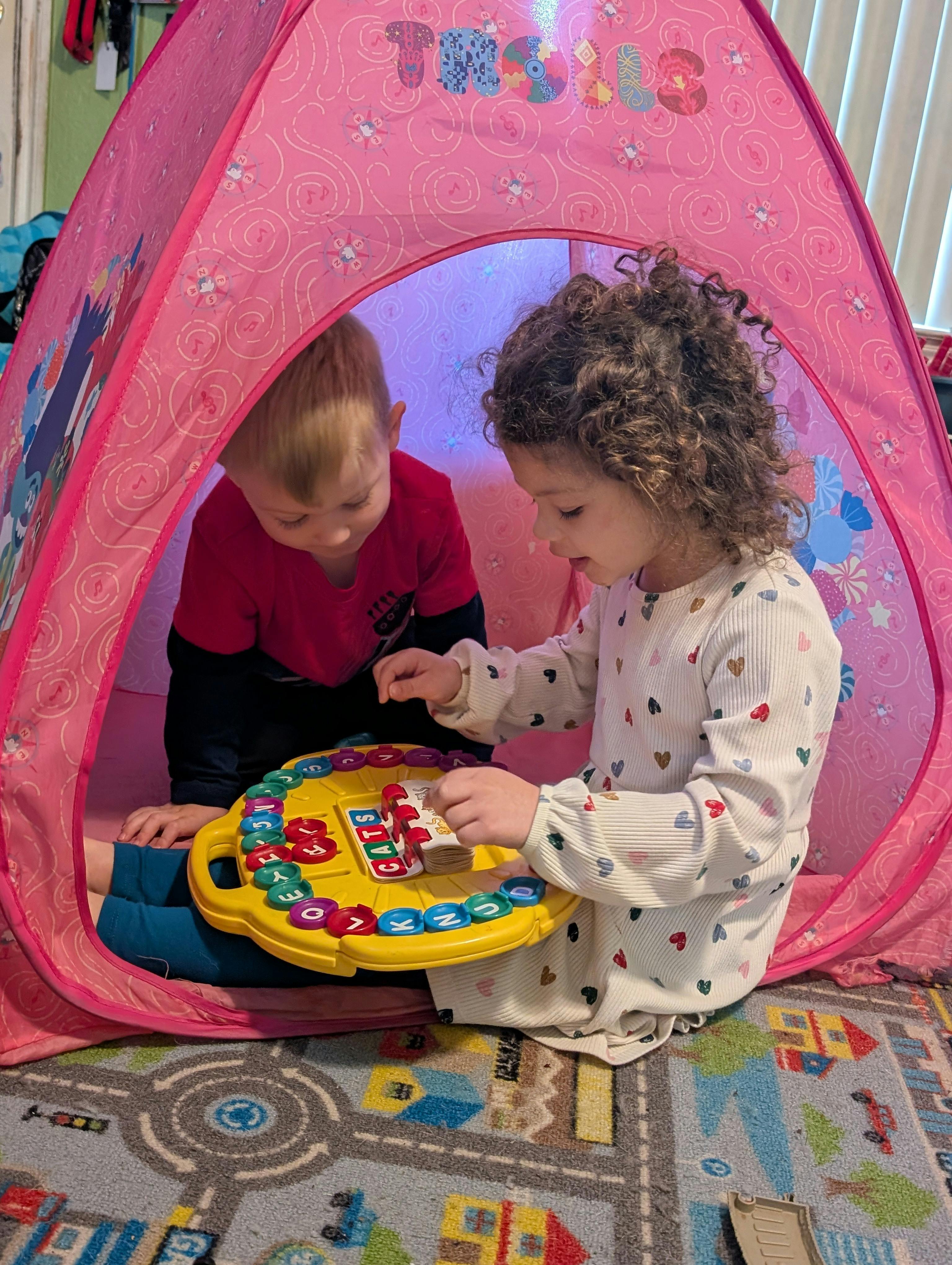 Two children playing with a letter board inside a pink tent