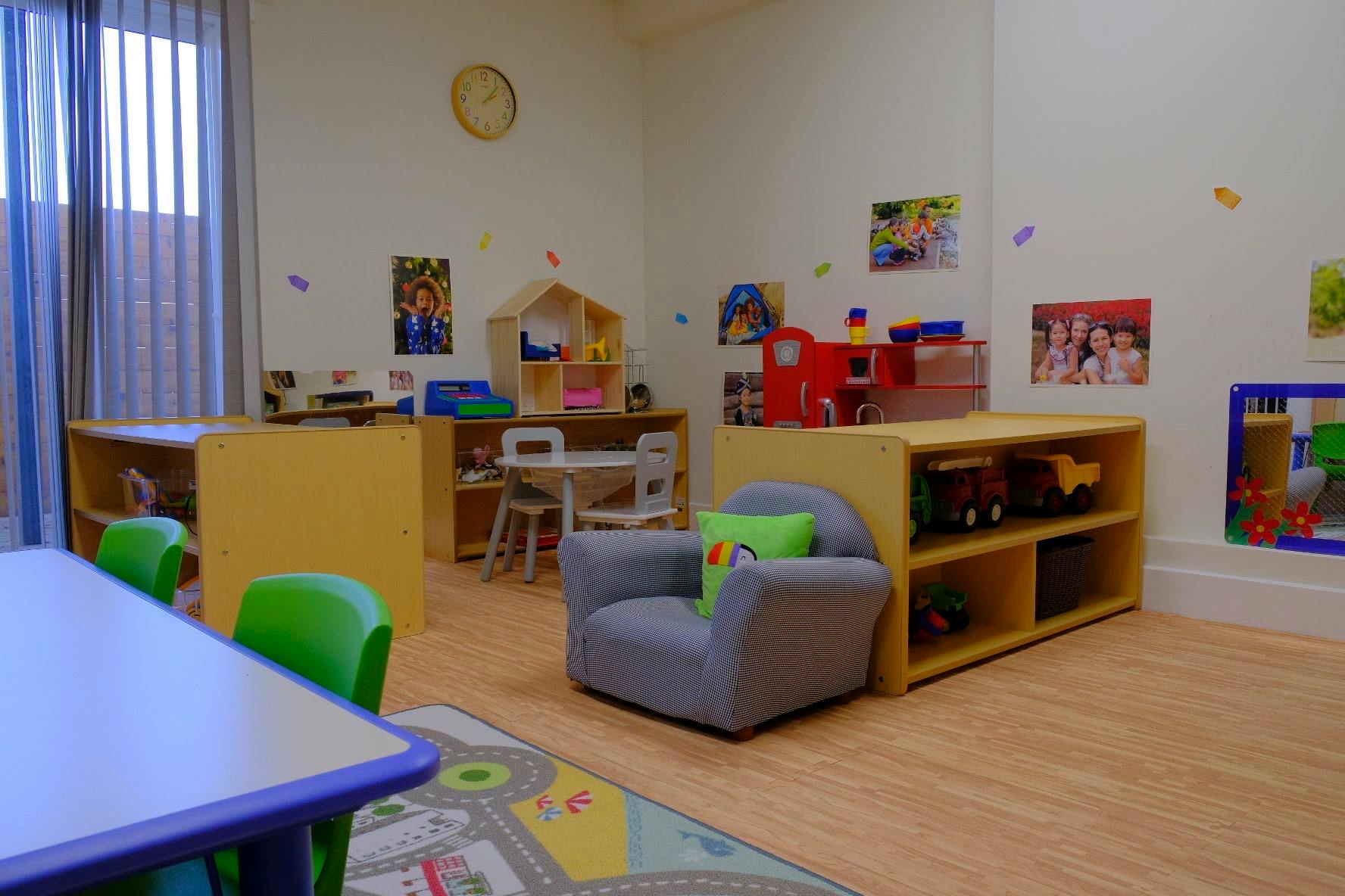 Playroom with small tables, chairs, shelves with toys, and a gray armchair
