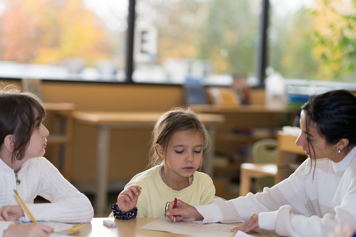 Adult and two children drawing at a table in a classroom