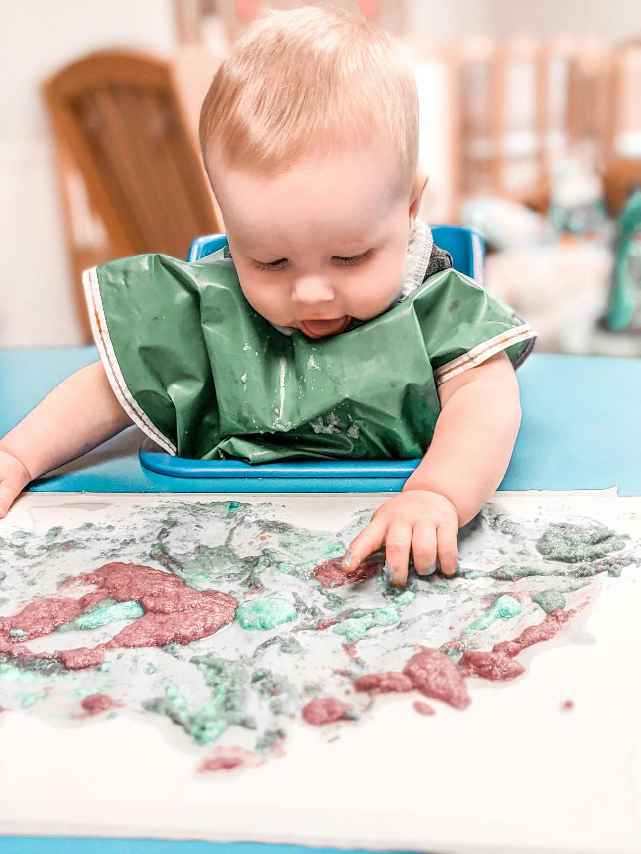 Child in a green bib finger painting with red and green paint