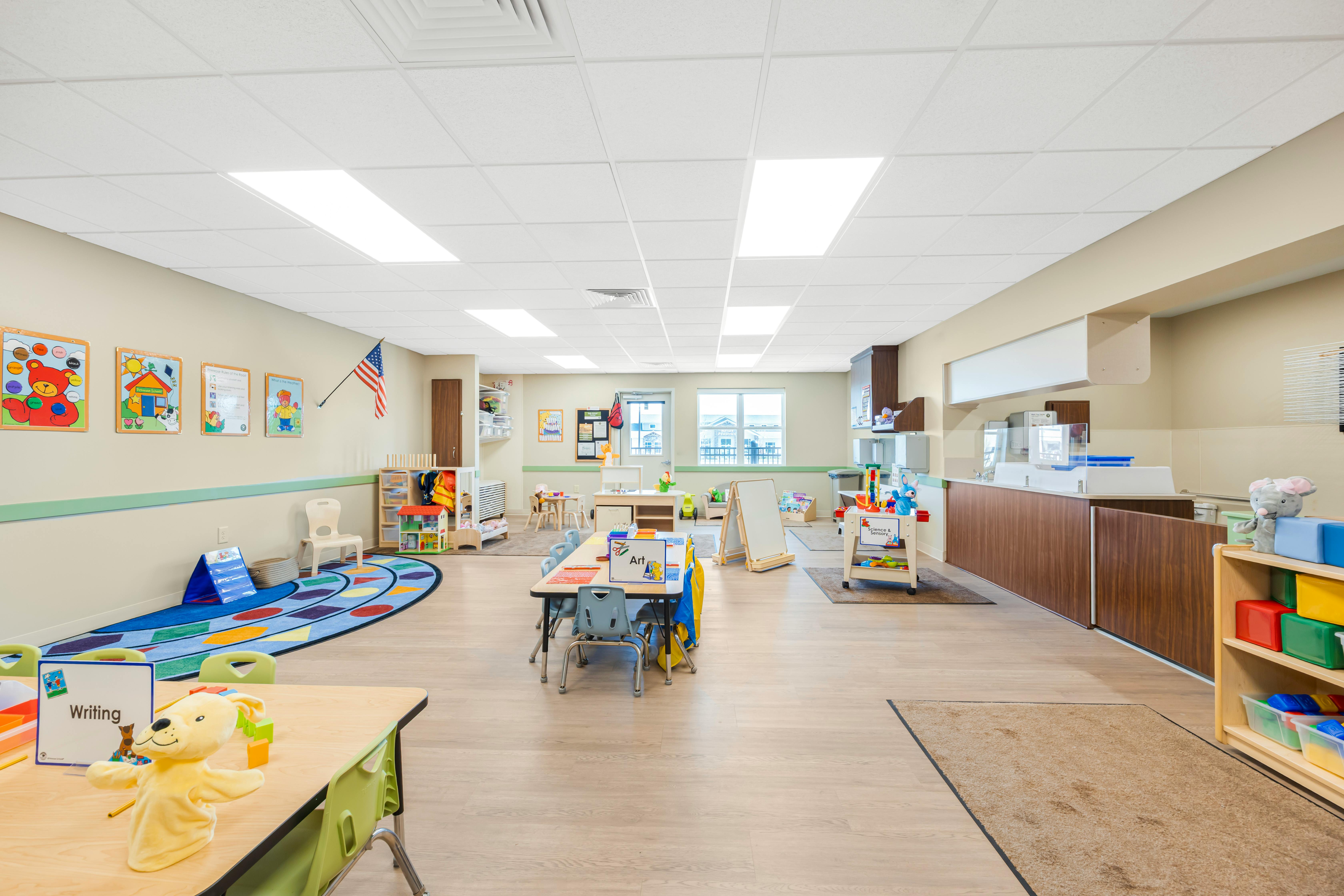 Empty classroom with small tables and chairs, toys, and educational posters on walls