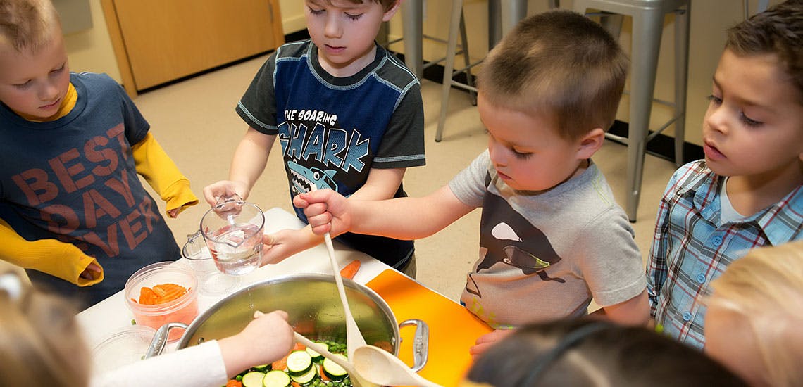 Children cooking with vegetables in a large pot