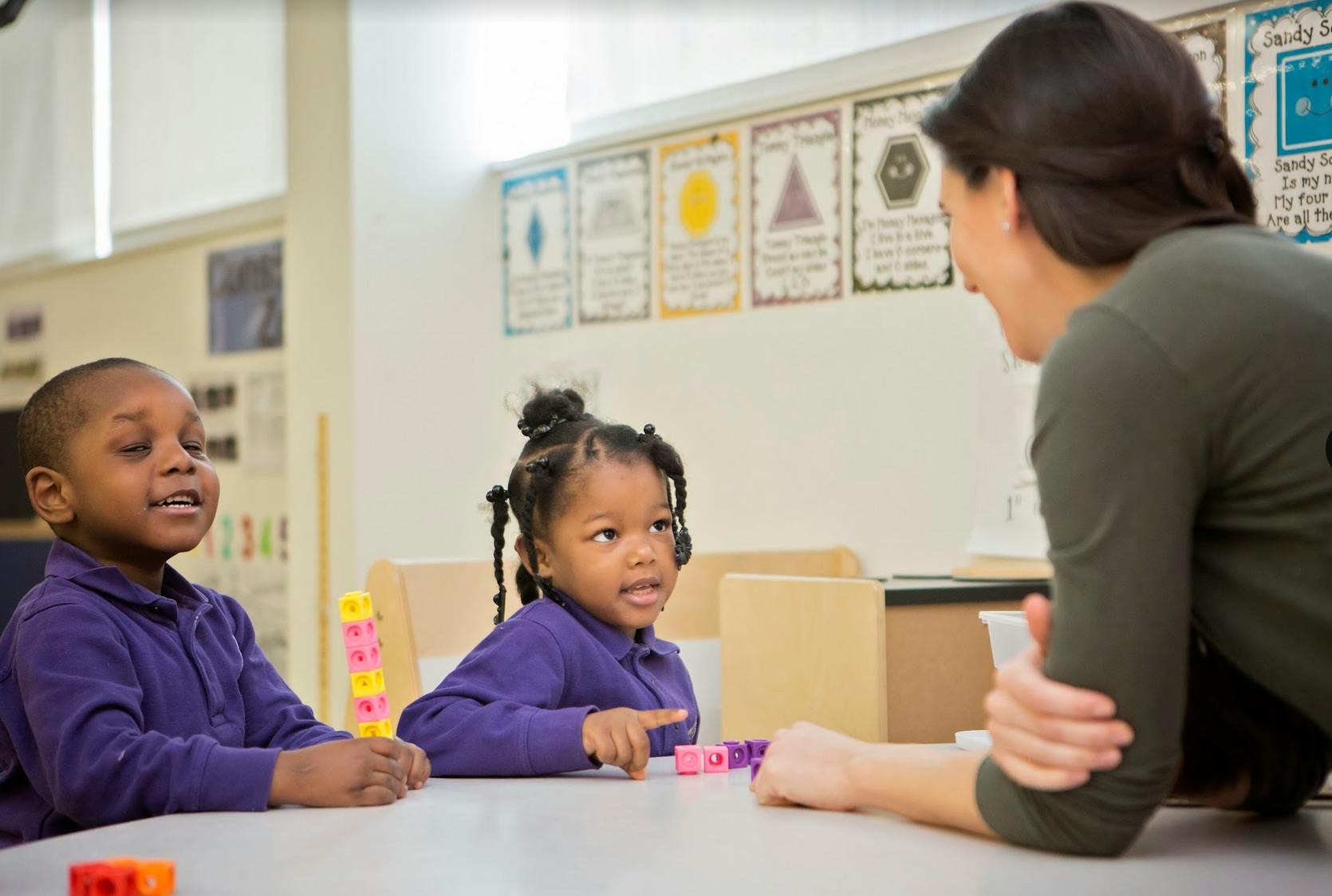 Two children and an adult interacting at a table in a classroom
