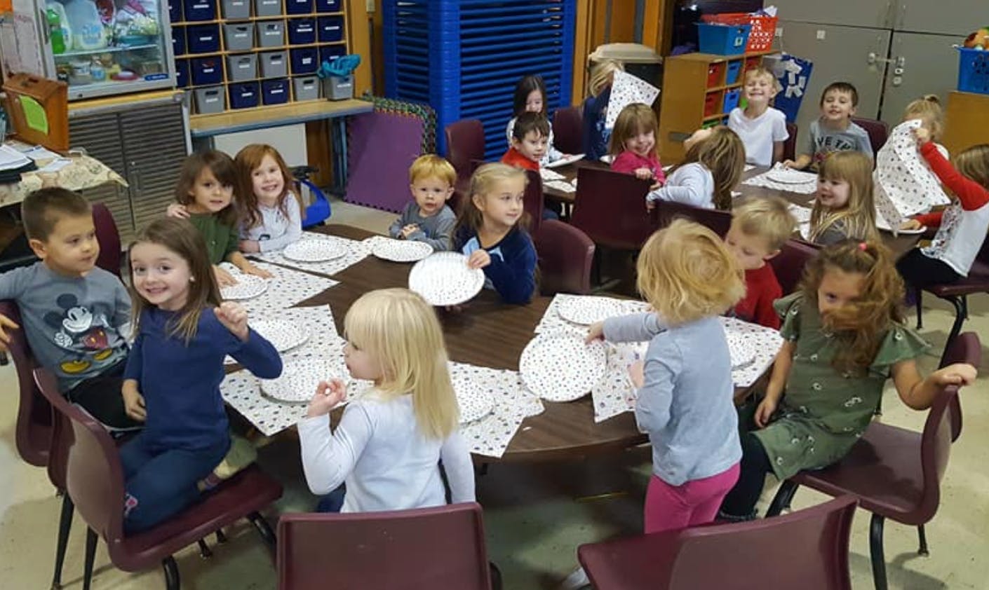 Children sitting at tables with plates in a classroom