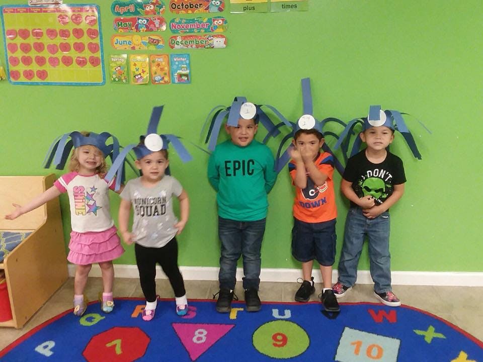 Five children wearing paper hats with antennae in a classroom