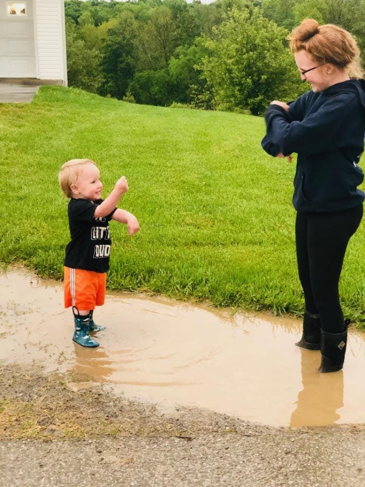Child and person in rain boots standing in a muddy puddle