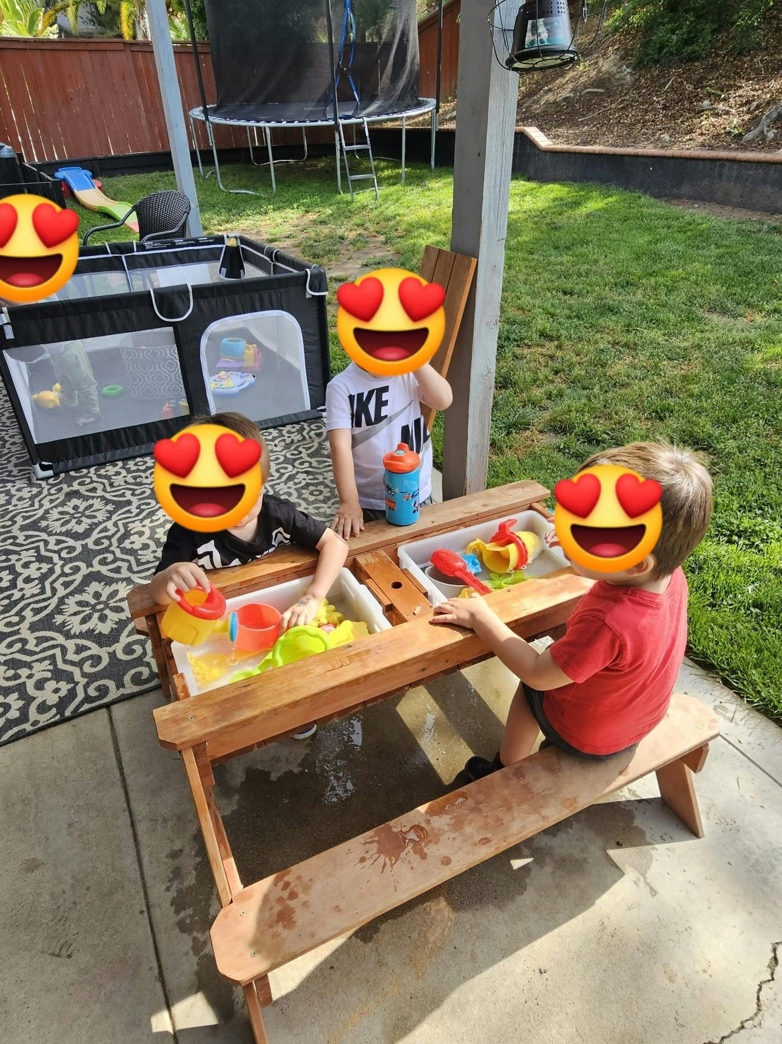 Three children playing at a wooden water table outdoors