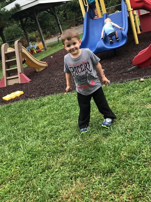 Child standing on grass in front of playground slide, and another child on, a playground slide