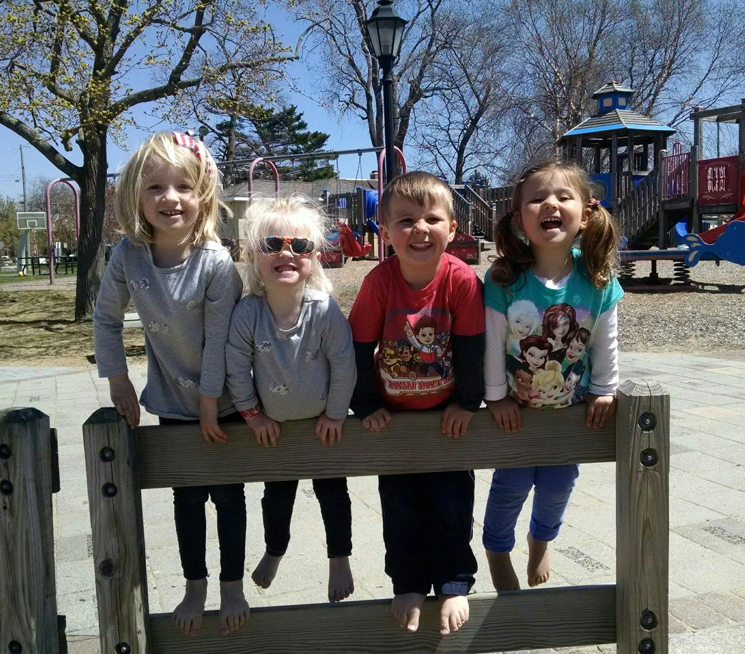 Four children sitting on a wooden fence at a playground