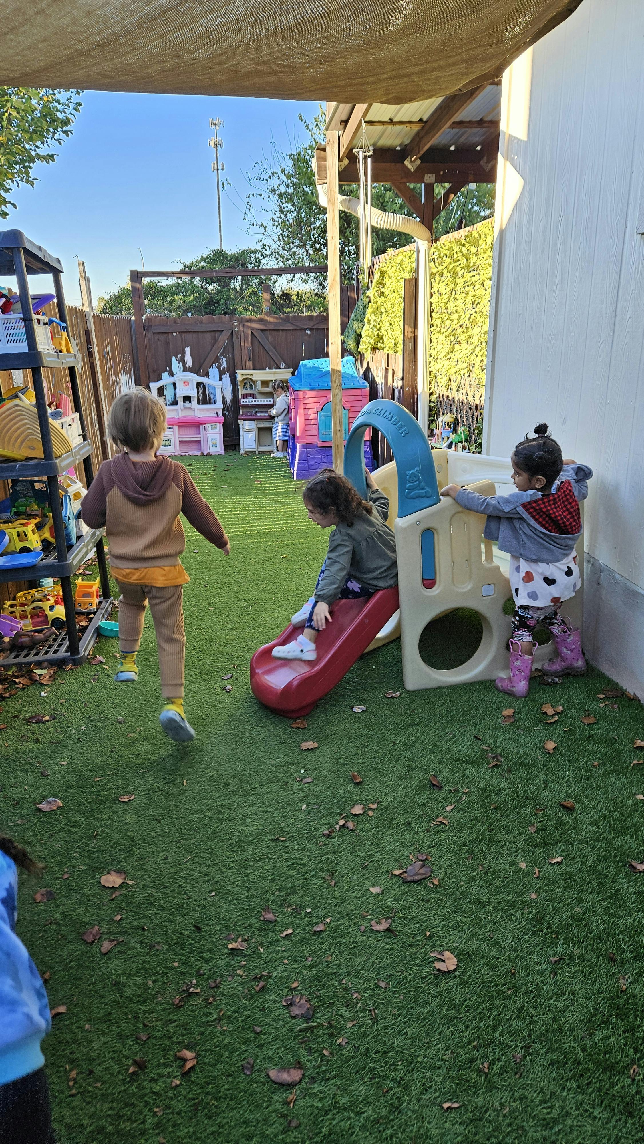 Three children playing on a slide and standing on artificial grass
