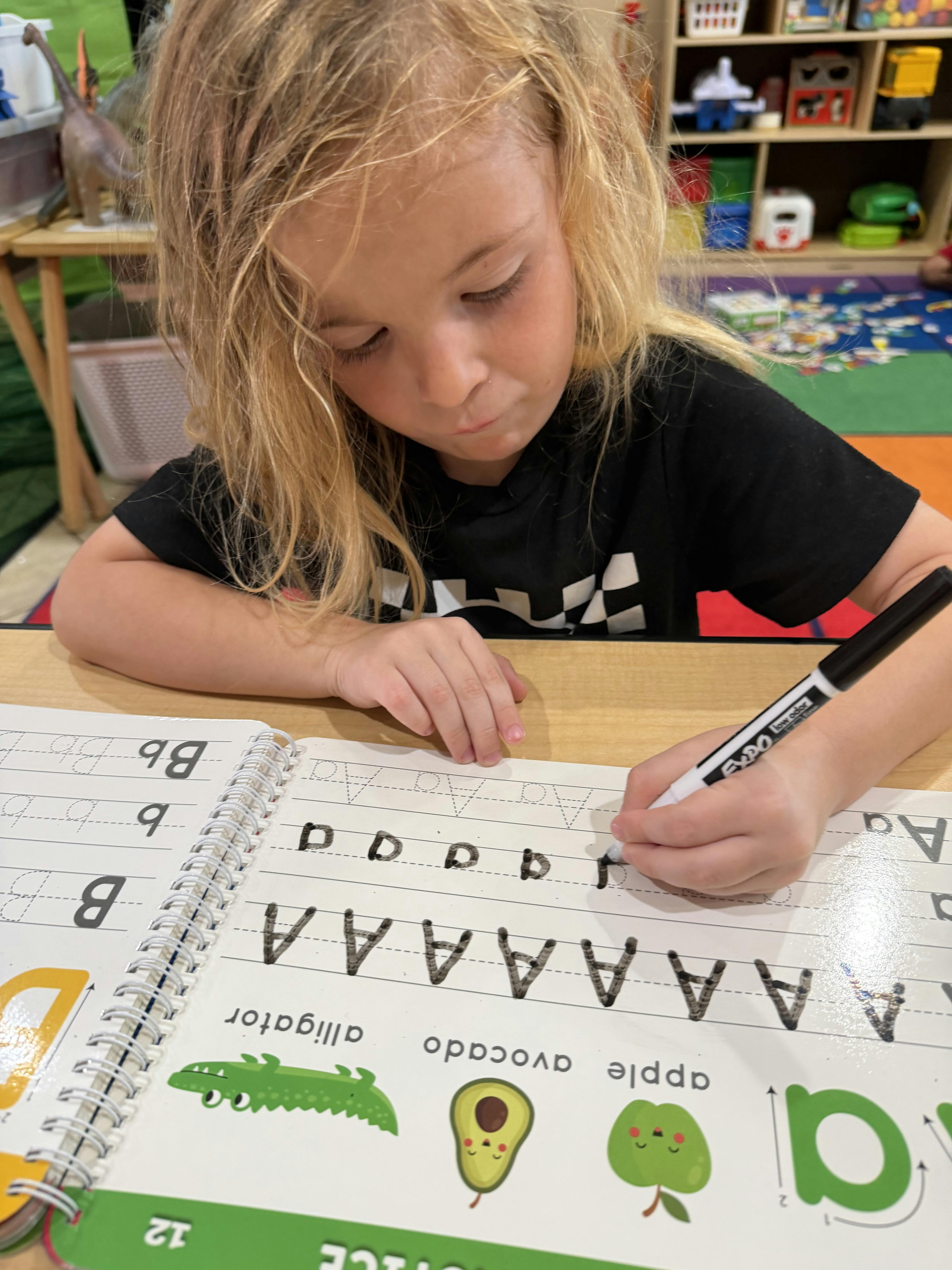 Child practicing writing letters in a workbook at a desk