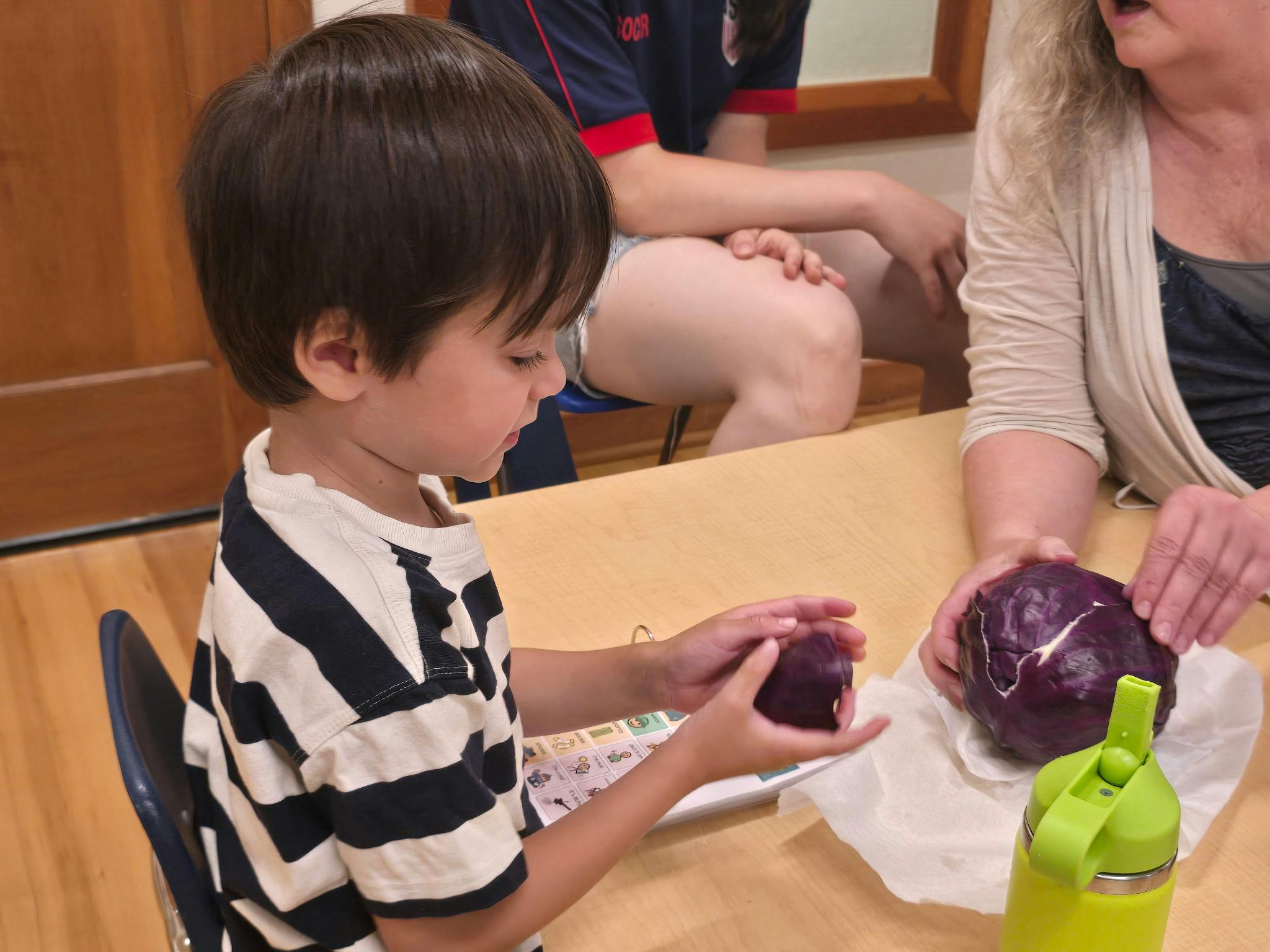Child handling a piece of red cabbage at a table with adults