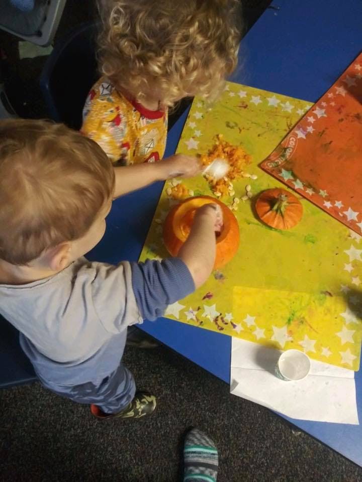 Two children carving pumpkins at a pumpkin on a table