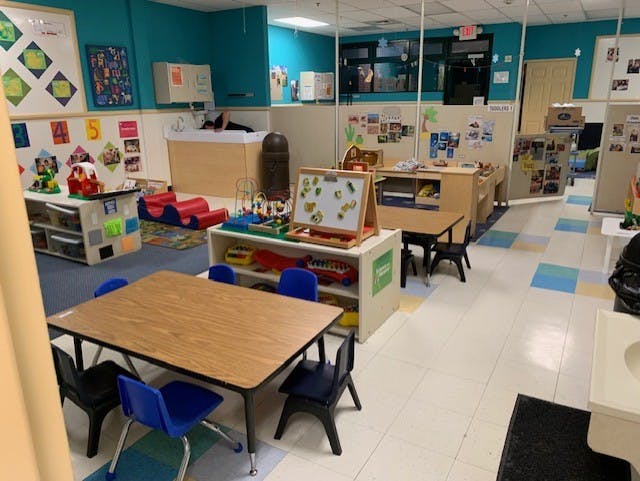 An empty children's classroom with small tables, chairs, and play areas