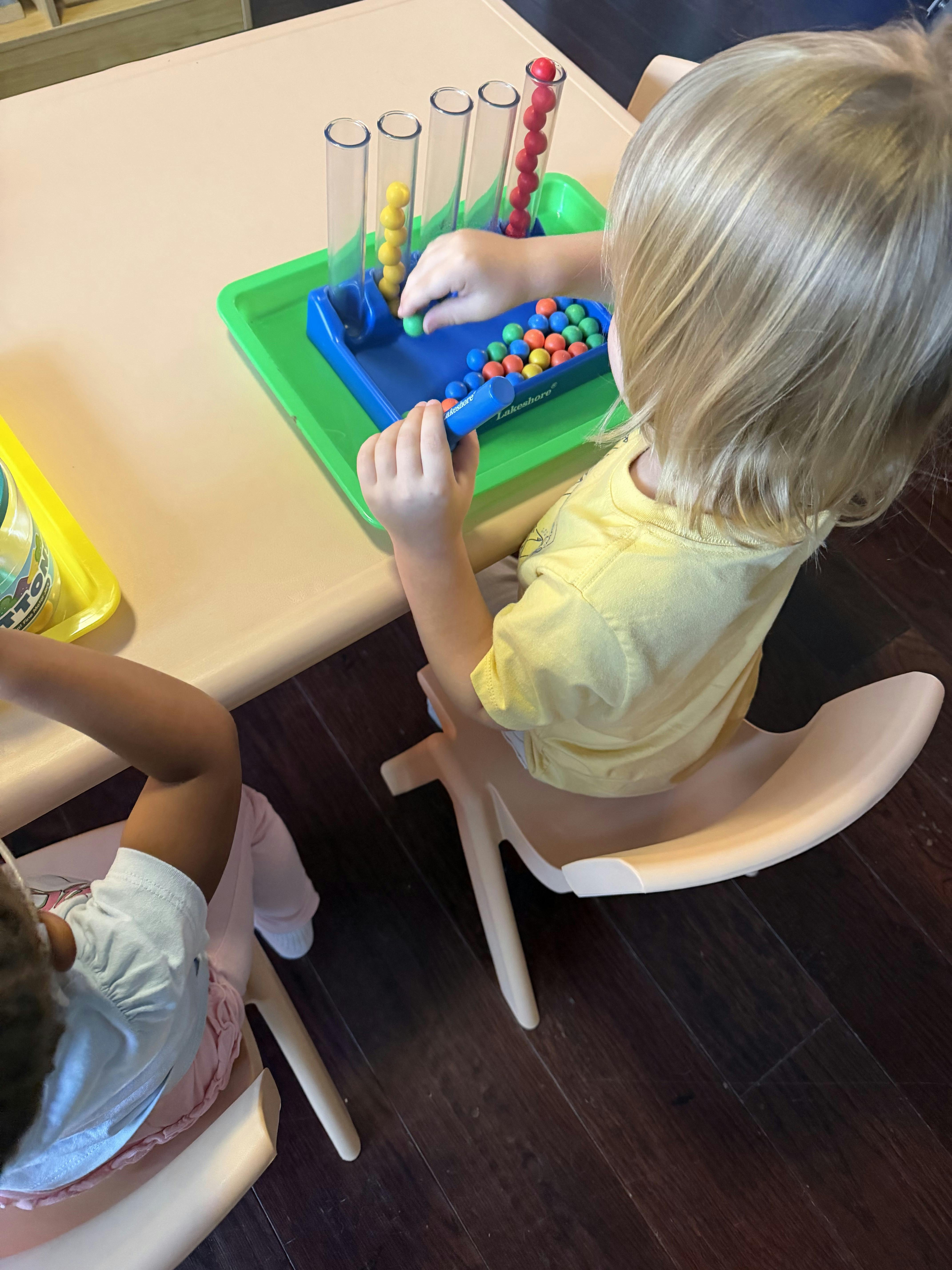Child placing small spheres into vertical plastic tubes