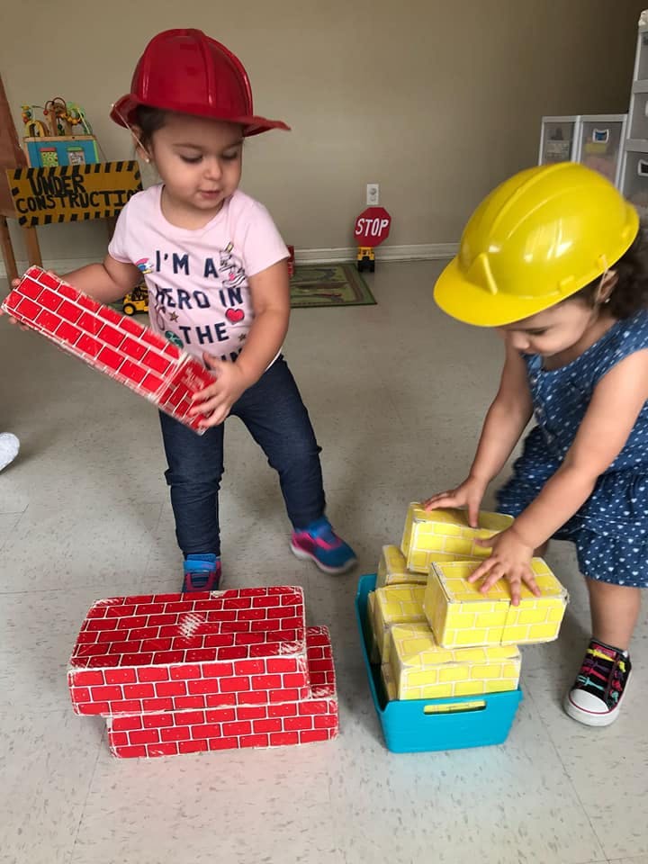Two children playing with toy bricks, one holding a red brick, one with yellow bricks