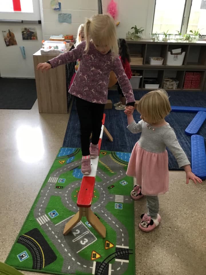 Child walking on a balance beam while holding another child's hand
