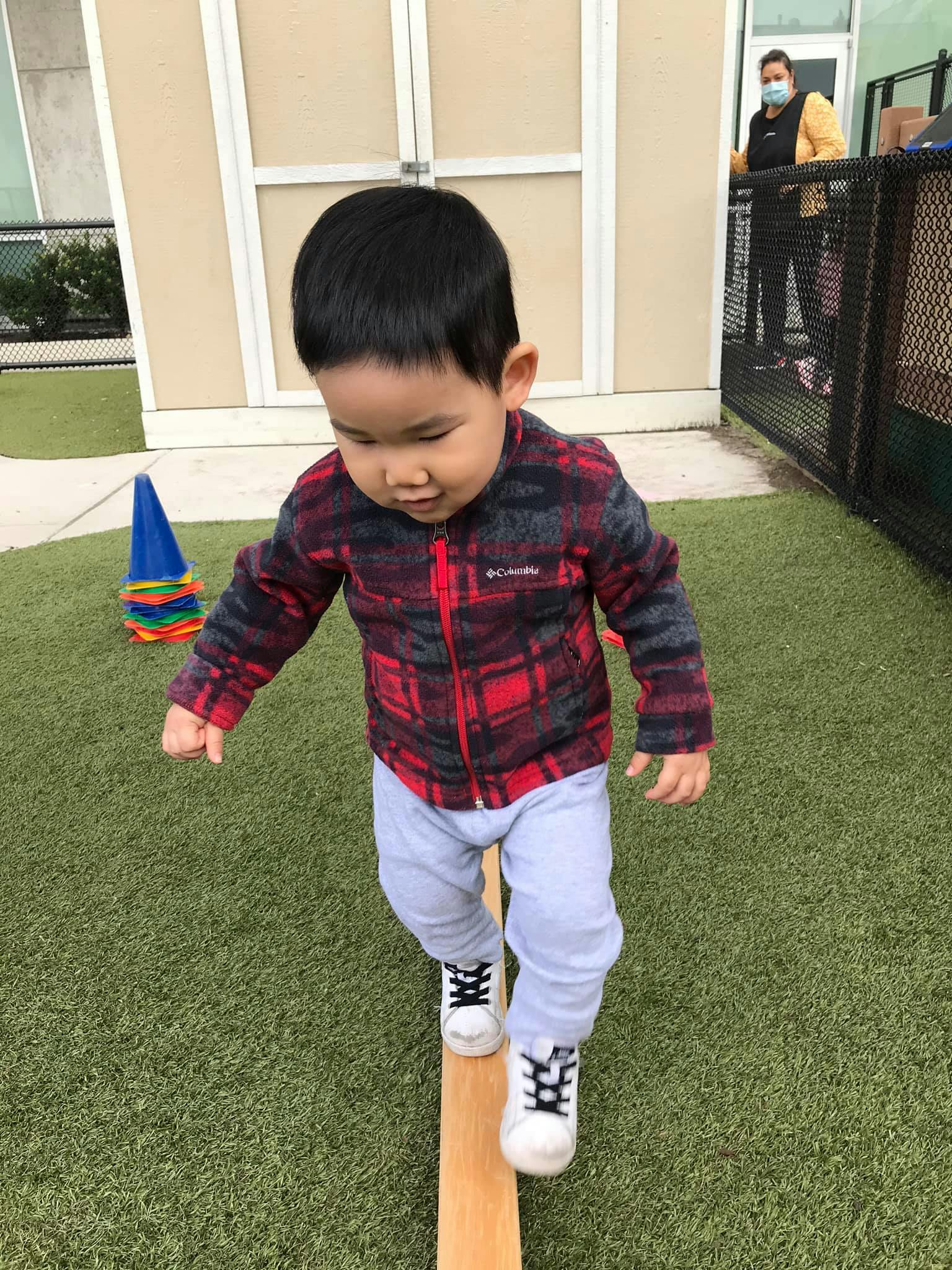 Child walking on a wooden beam on artificial grass