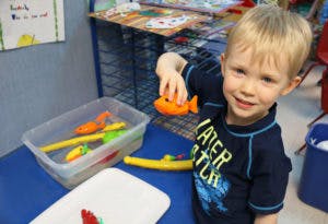 Child holding an orange toy fish over a bin of water and toys