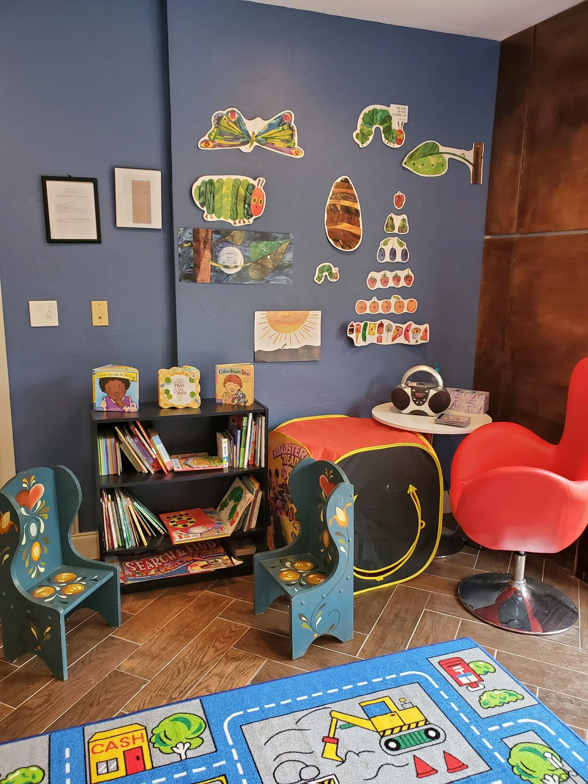 Children's play area with bookshelf, chairs, and wall decorations
