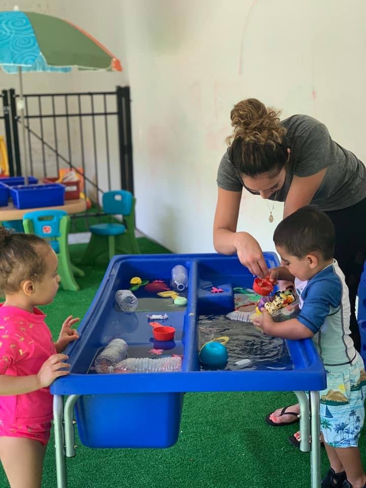 Adult and two children playing with toys in a water table