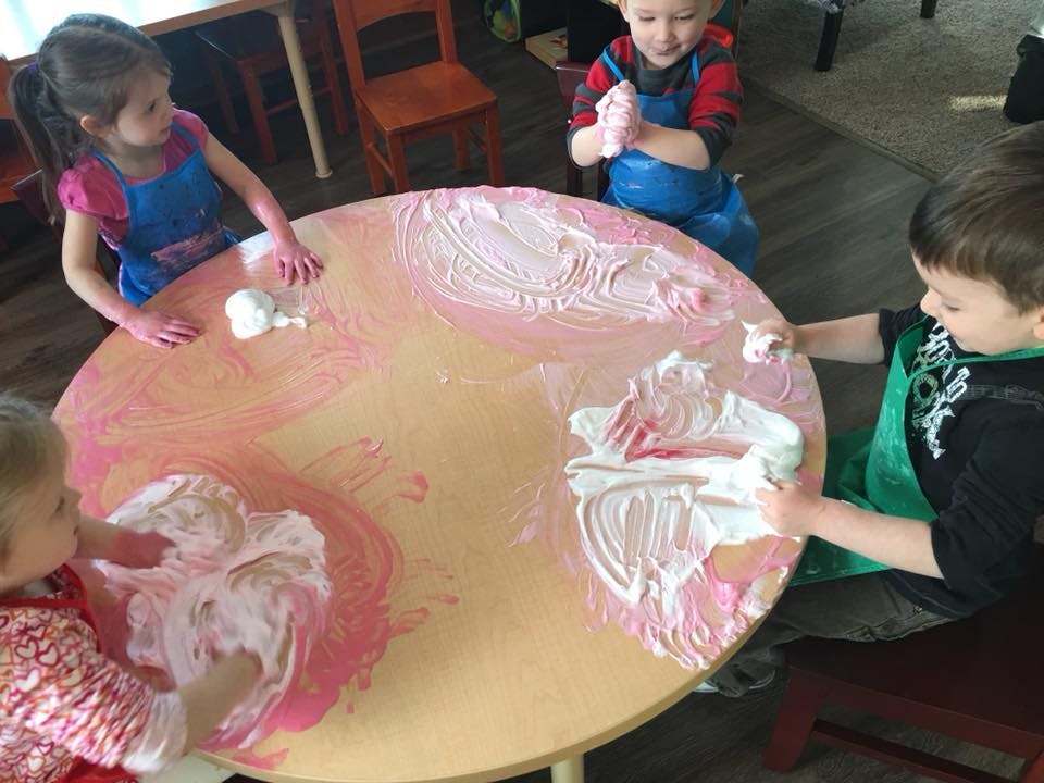Children playing with shaving cream and paint on a table