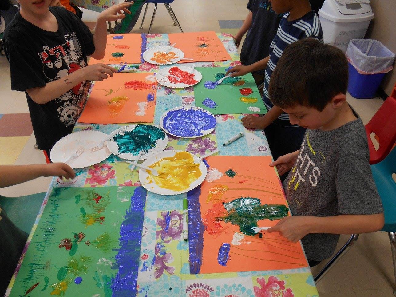 Children painting with colorful paints on paper at a table