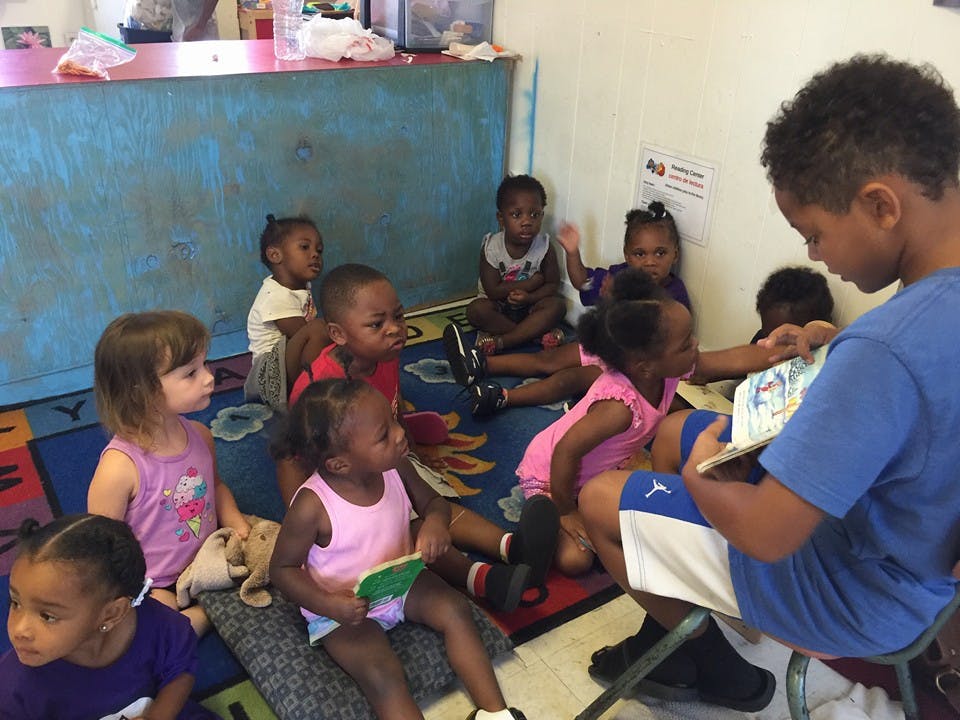 Teen reading a book to a group of children sitting on a rug