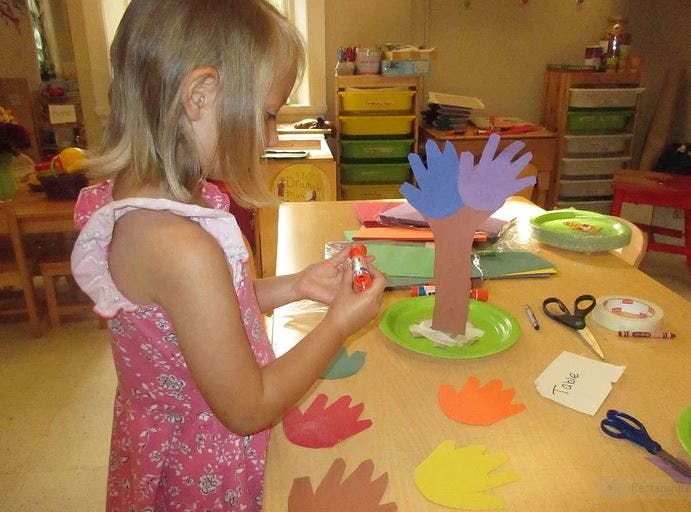 Child making a craft tree with paper hand cutouts