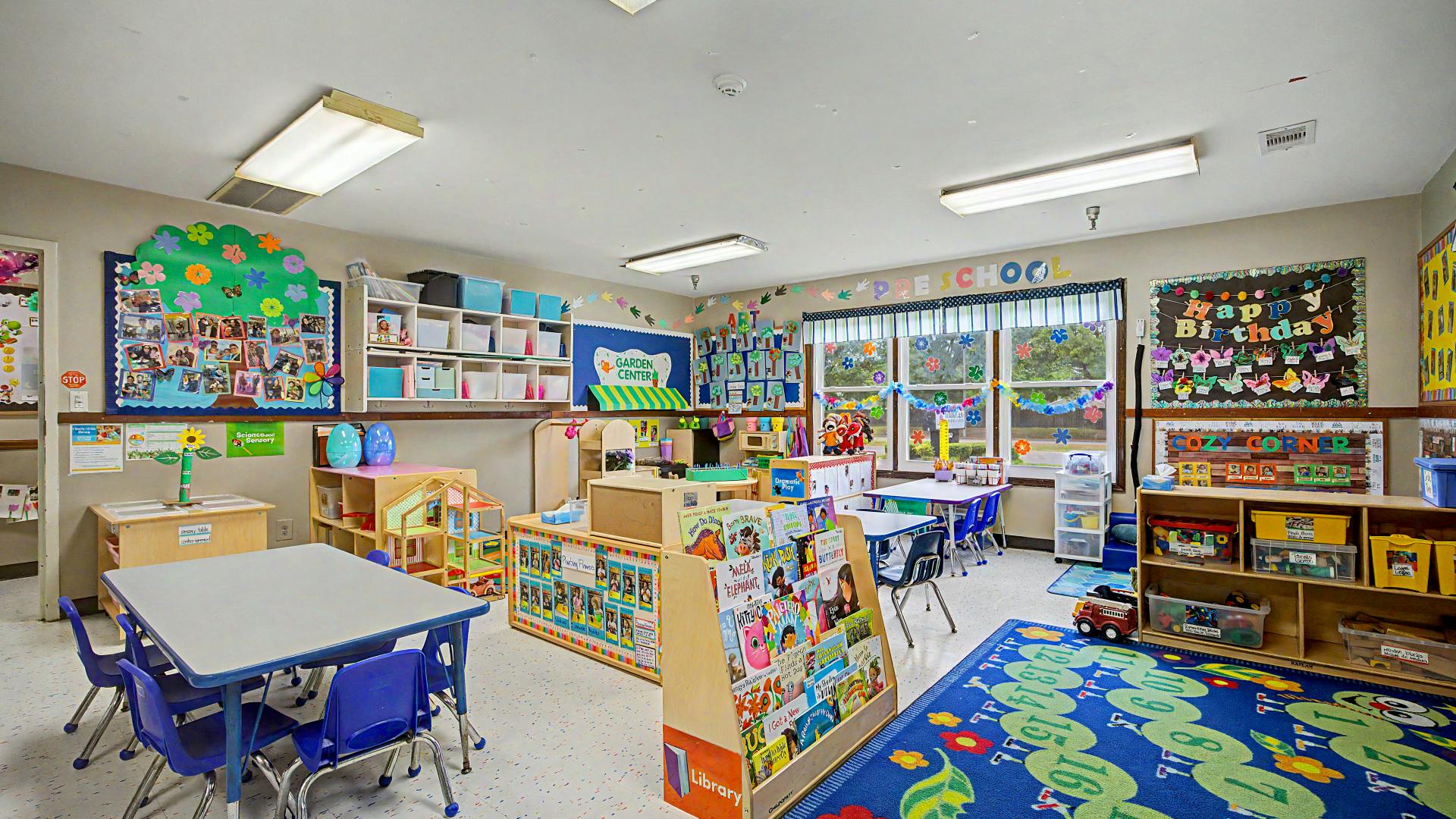 Colorful preschool classroom with various learning centers, tables, and a book display