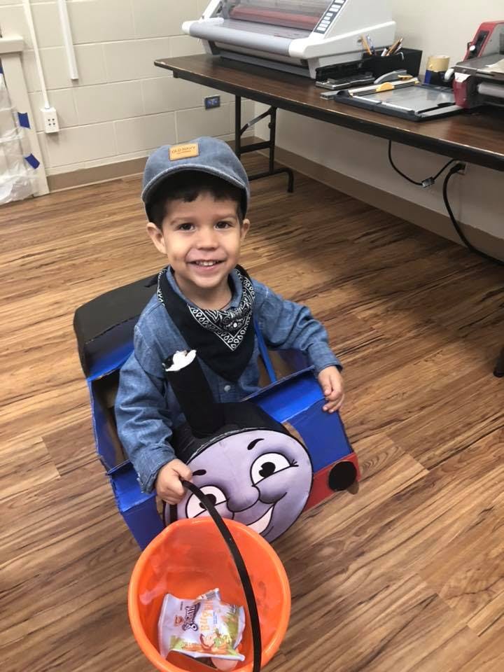 Child in a train costume holding an orange bucket