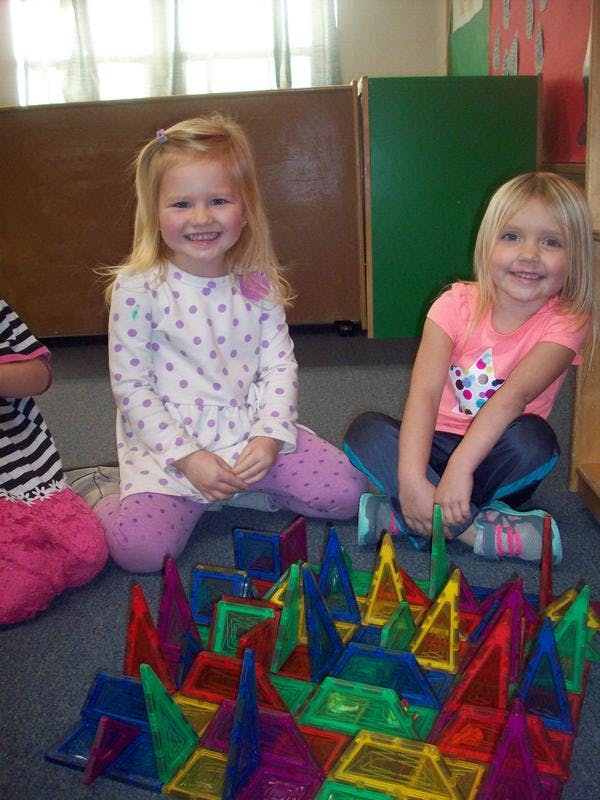 Two children sitting on the floor with colorful magnetic tiles