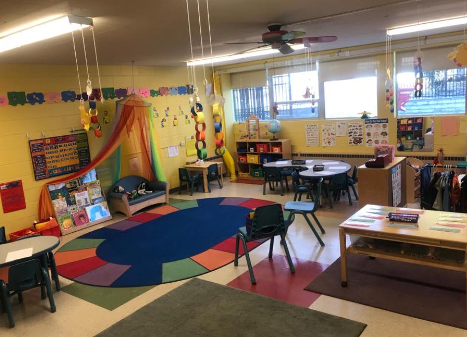 Classroom with colorful rug, small tables and chairs, and a reading nook