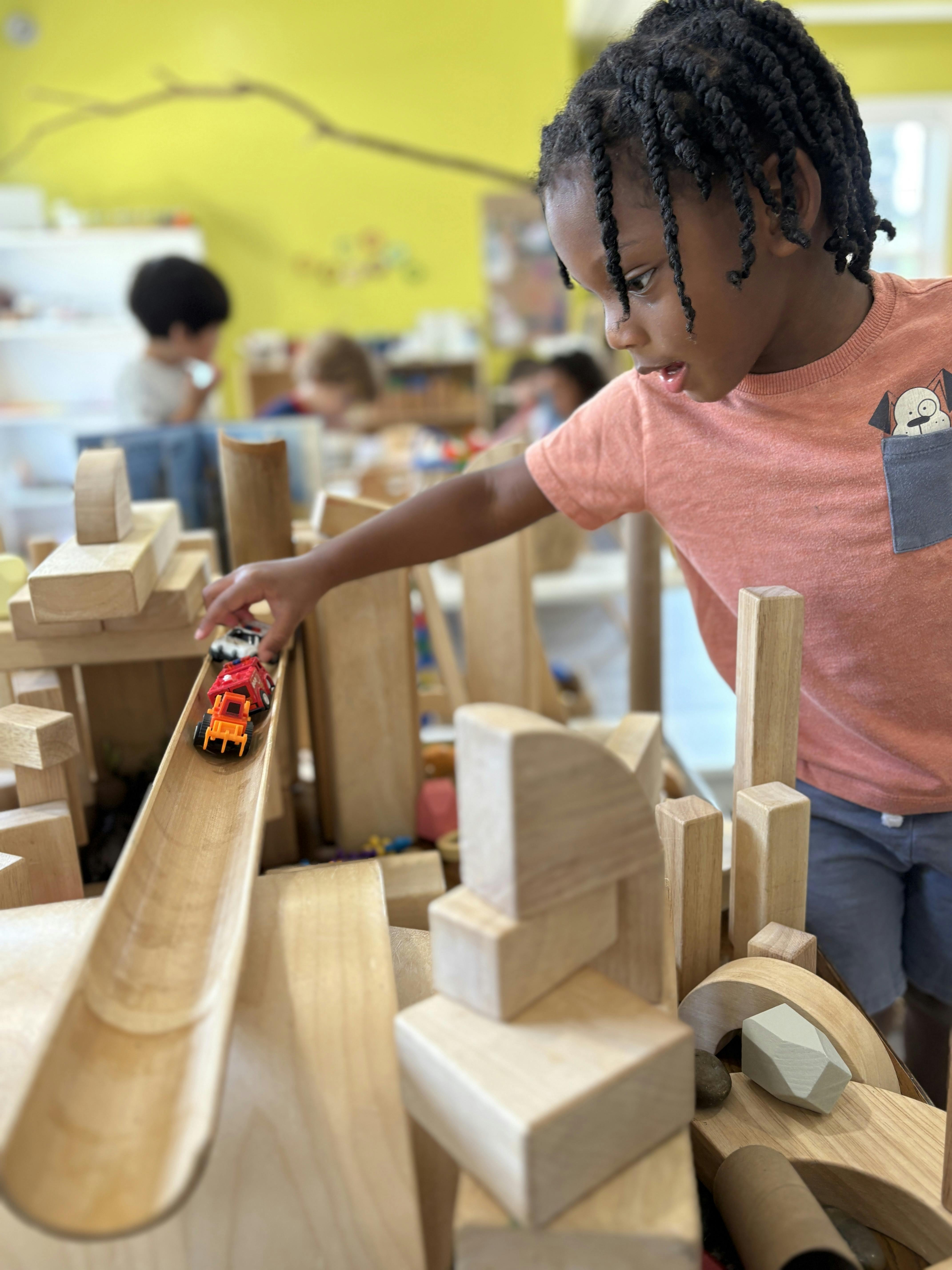 Child playing with wooden blocks and toy cars in a classroom