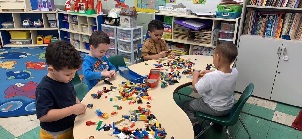 Four children playing with building blocks at a table in a classroom