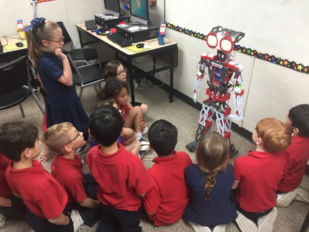 Children sitting on floor looking at a robot in a classroom